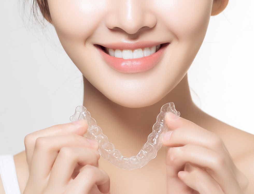 투명 교정장치를 손에 들고 치아에 끼우는 모습을 보여주는 여성